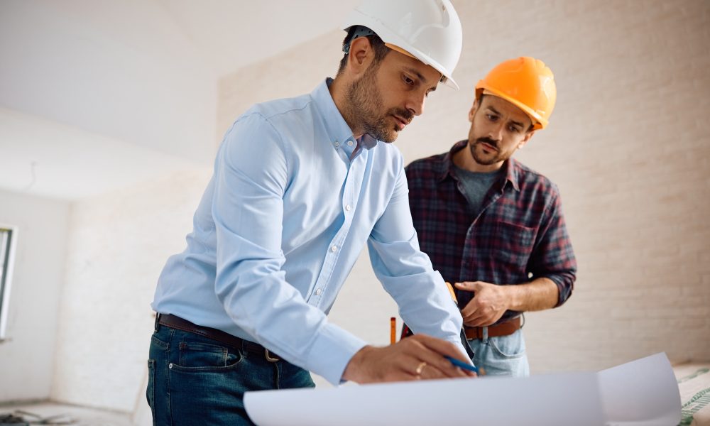 Architect and construction worker analyzing blueprints during home remodeling project.