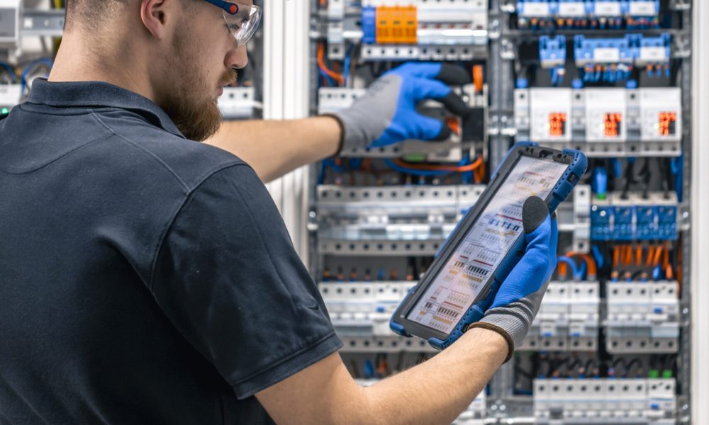 Electrical technician working in a switchboard with fuses, uses a tablet. Electrical technician looking focused while working in a switchboard with fuses.
