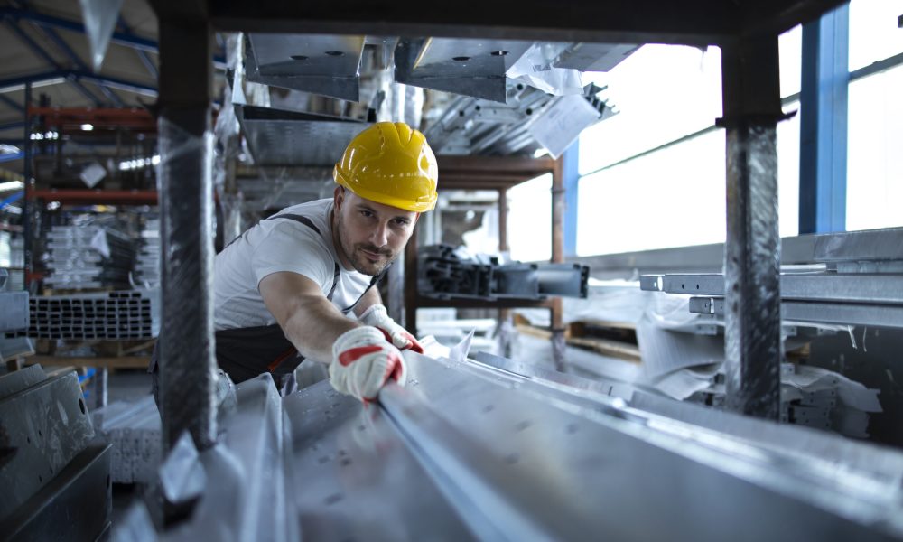 Factory worker working in warehouse handling metal material for production.
