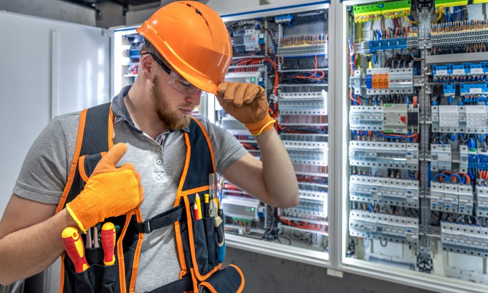 Male electrician working in electrical panel. Male electrician in uniform. High quality photo. Male construction worker in helmet and safety glasses.