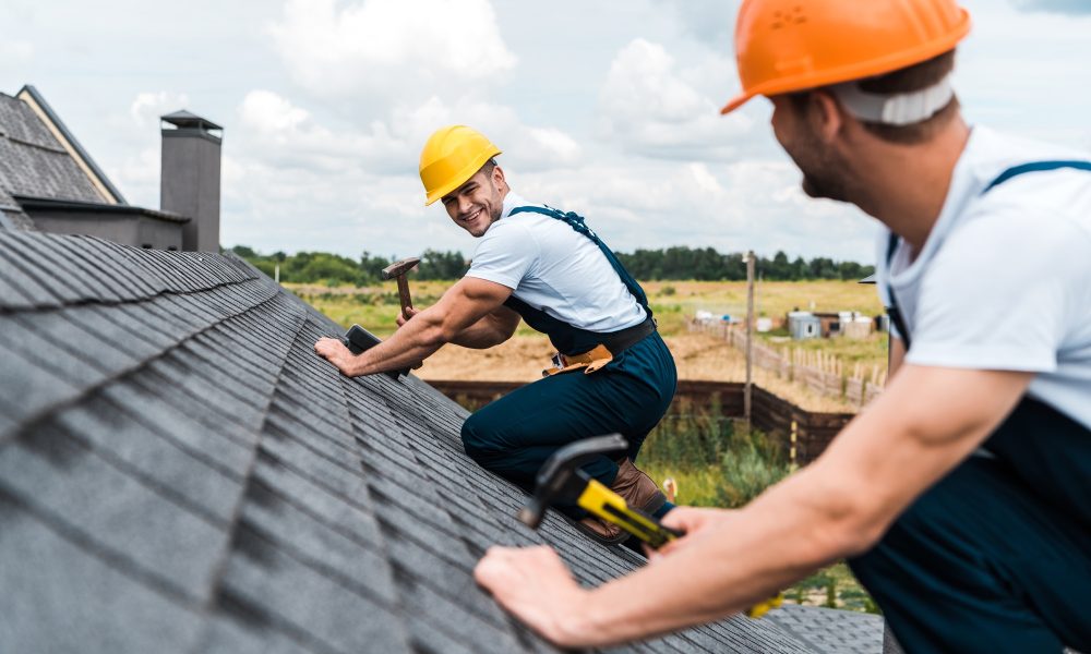 selective focus of happy repairman looking at coworker on roof